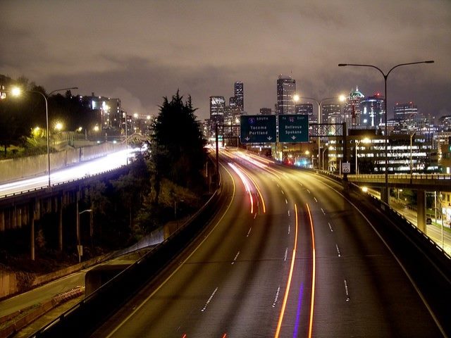 Nighttime view of highway with city skyline in background.