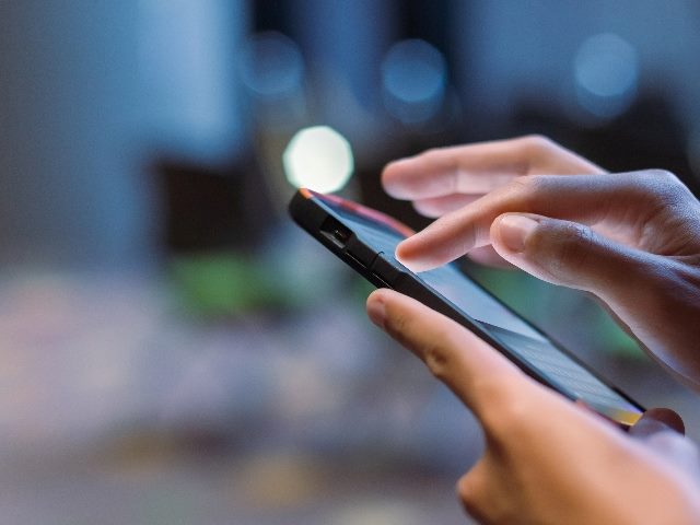 Close-up male hand using smartphone at meeting room blurred background suggesting the importance of DXPs in Omnichannel Experience. 
