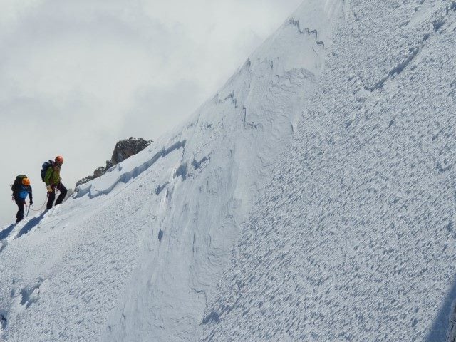 Two mountain-climbers facing a steep ascent on a snow-covered mountain.