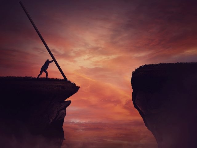 Businessman in the distance pushing a long beam, creating an improvised bridge to cross the abyss obstacle.