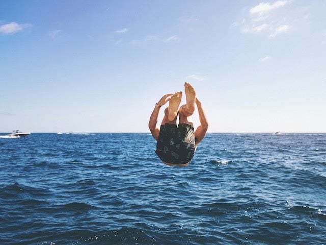 man doing a backflip into the ocean, boat in the distance