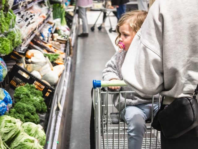 A young child shopping with her mother at the supermarket in New Zealand, looking at vegetables. 