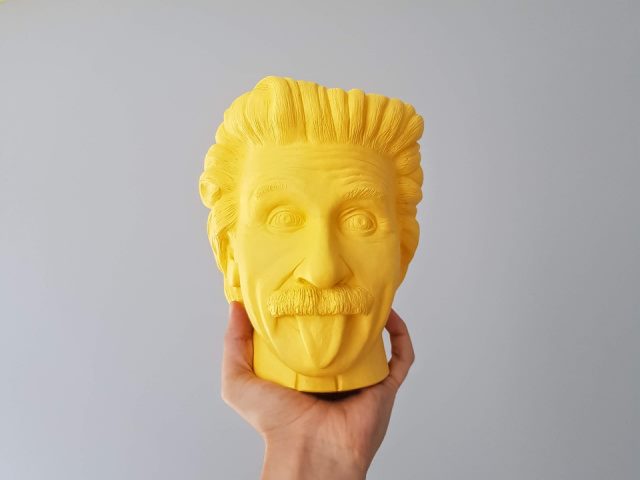 yellow Albert Einstein bust behind held up in a person's hand