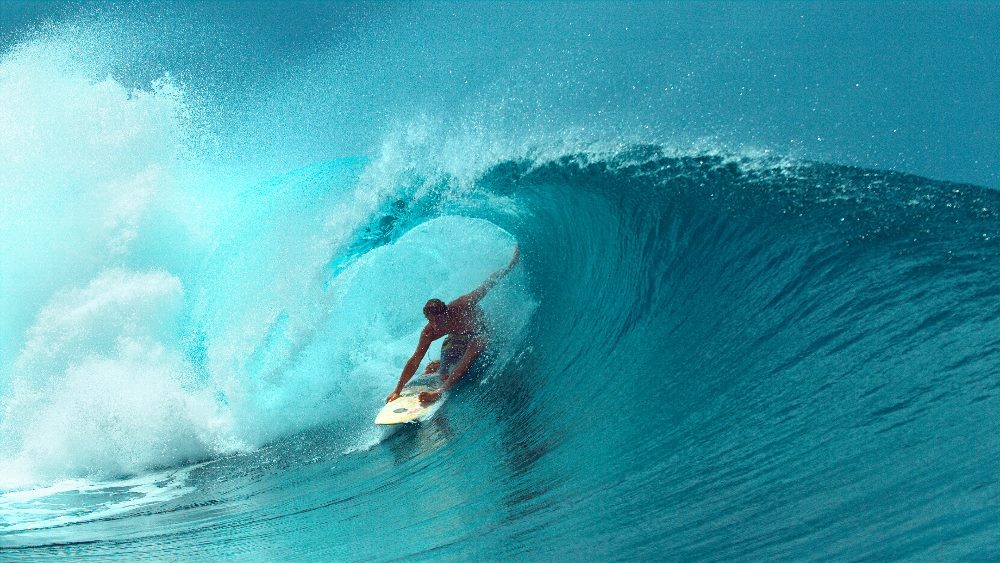 A surfer is riding a powerful, curling wave. The ocean's vibrant blue and turquoise colors highlight the dynamic movement of the water. The surfer, poised and focused, navigates the wave expertly, emphasizing both the challenge and exhilaration of the activity. The scene captures the essence of surfing with a clear sky in the background and the sun reflecting off the water in piece about UX design.