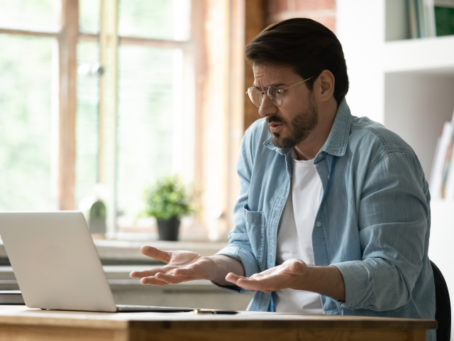 An unhappy and irritated businessman in glasses looking at laptop screen.