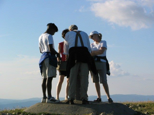 Four people gather in a huddle on top of a hilltop or mountain