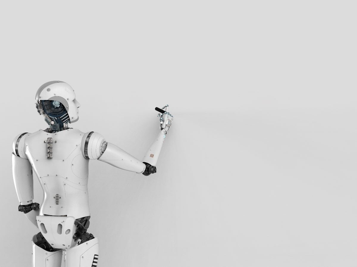 White humanoid robot seen from behind, extending its arm to write or draw on a blank gray wall, symbolizing AI-generated content and automation.