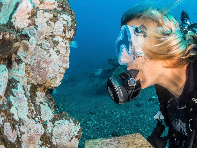 scuba diver coming up against a statue underwater