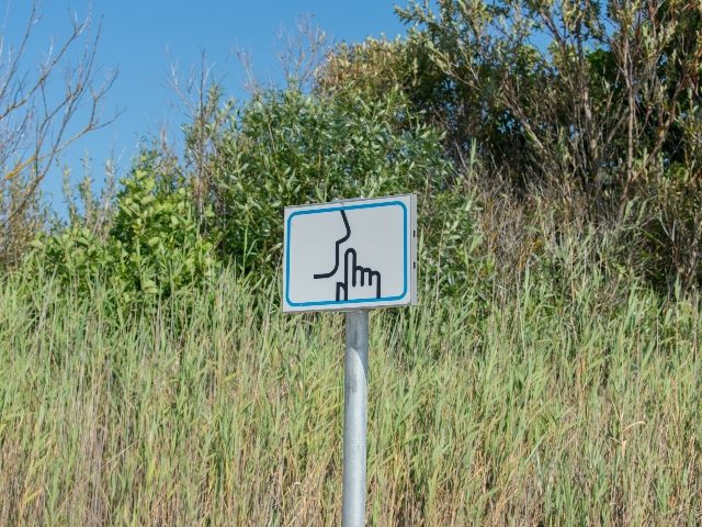 Signpost with be keep quiet/silent please sign. Green plants in the background.