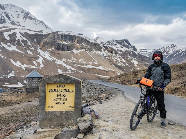 man paused on bicycle part of the way up snow covered mountains in India