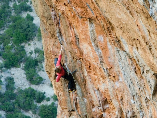 woman climbing  up the face of a steep rock in Greece