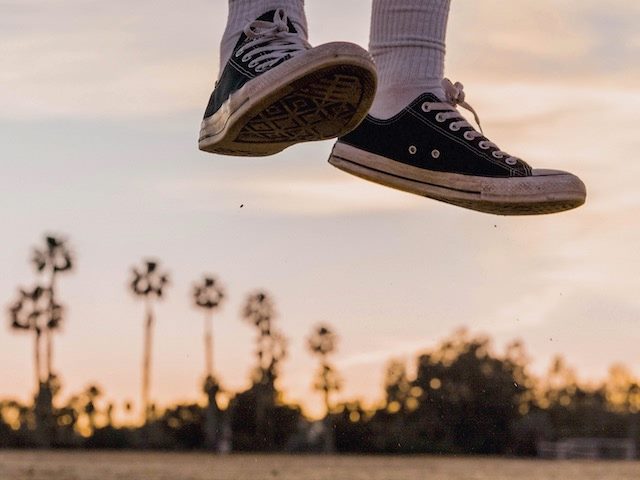 person's sneaker-clad feet caught mid-jump, palm trees and beach scene in background