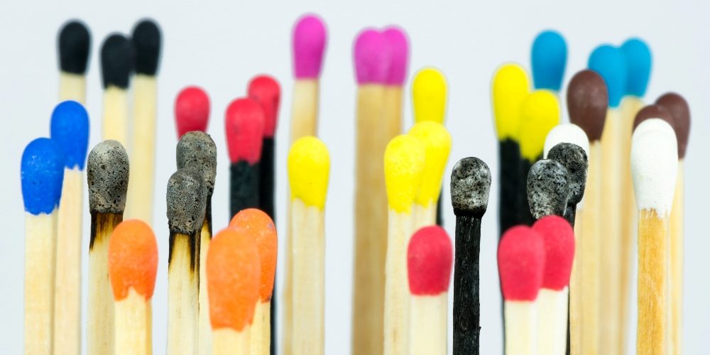 Wooden match heads of various colors, including red, blue, yellow, green, magenta, white, brown and black with some matches having been lit and burned in piece about lazy girl marketing strategies.