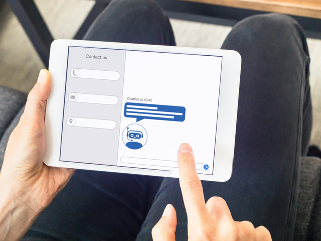 A person interacting with a chatbot with artificial intelligence technology (AI) internet virtual assistant on digital tablet computer screen