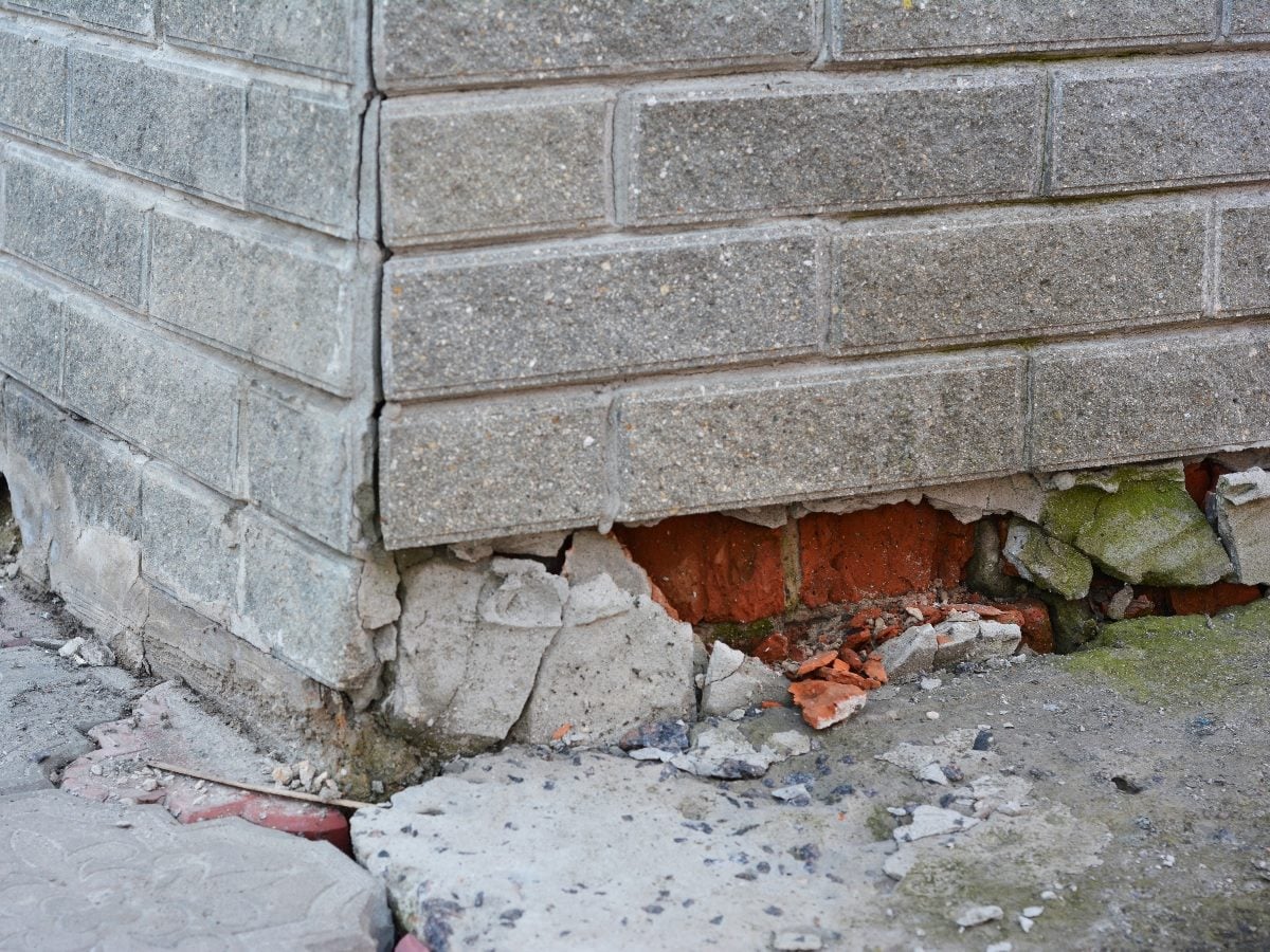 Damaged brick building corner with cracked masonry and exposed foundation bricks, illustrating a fragile structural layer beneath the surface.