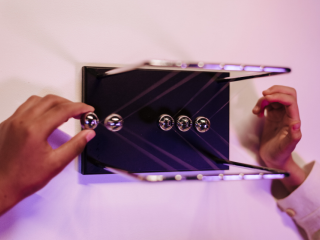 Two hands work a Newton' s Cradle, while looking down at the hanging balls - business alignment concept
