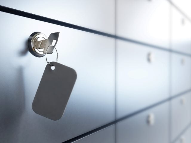 A key hangs from a keyhole in a row of gray bank safety deposit boxes.