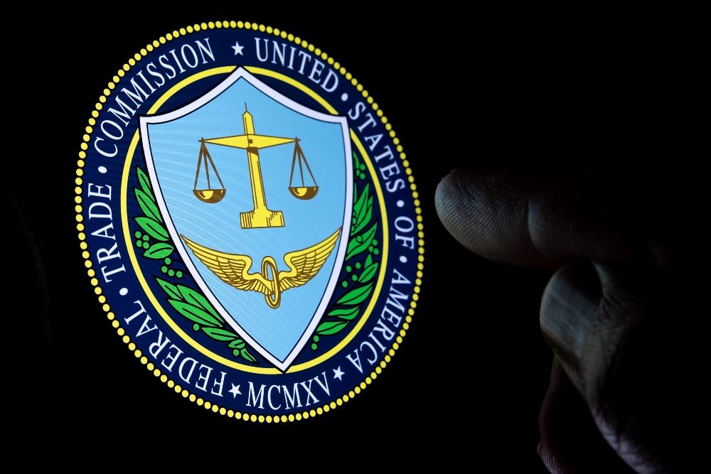 FTC Federal Trade Commission of the United States of America logo seen on the display in a dark room and blurred finger pointing at it in piece about the FTC's Google antitrust case.