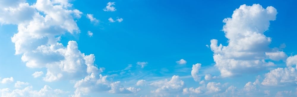 Panorama of a beautiful blue sky and white puffy clouds in piece about hybrid clouds and data automation.