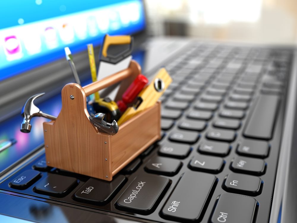 A tiny old-fashioned wooden toolbox filled with tools such a saws, hammers, screwdrivers and the like sits atop a computer keyboard in piece about building customer advocacy.