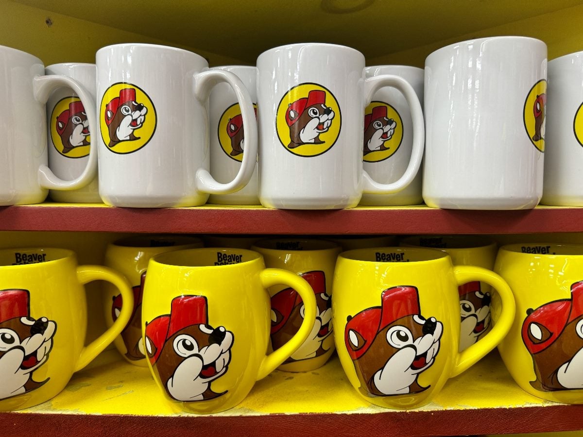 Shelves of Buc-ee’s branded coffee mugs featuring the smiling beaver mascot in a red cap, displayed inside a Buc-ee’s travel center store in Temple, Texas.