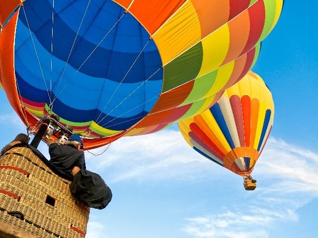 A closeup of a hot air balloon and balloonist with another visible in the background, the balloons are brightly colored with baskets hanging beneath in piece about ChatGPT's new GPT Mentions feature.  