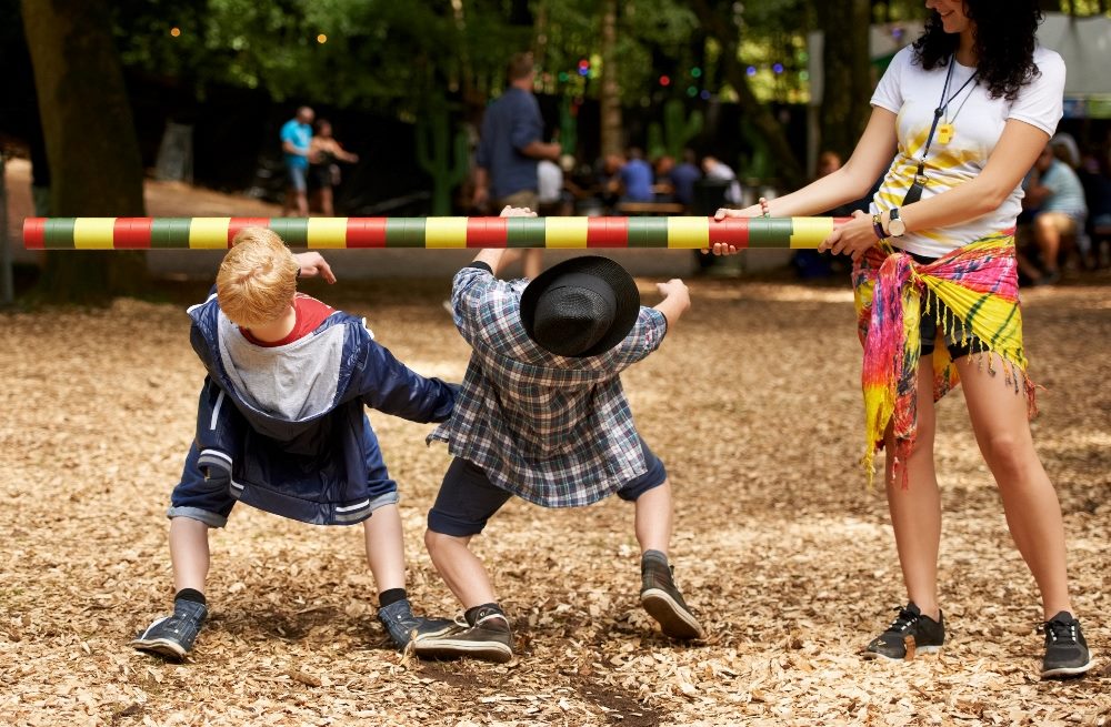 Two kids doing the limbo with a yellow and red beribboned pole at an outdoor festival in piece about AI customer experience and AI integration.