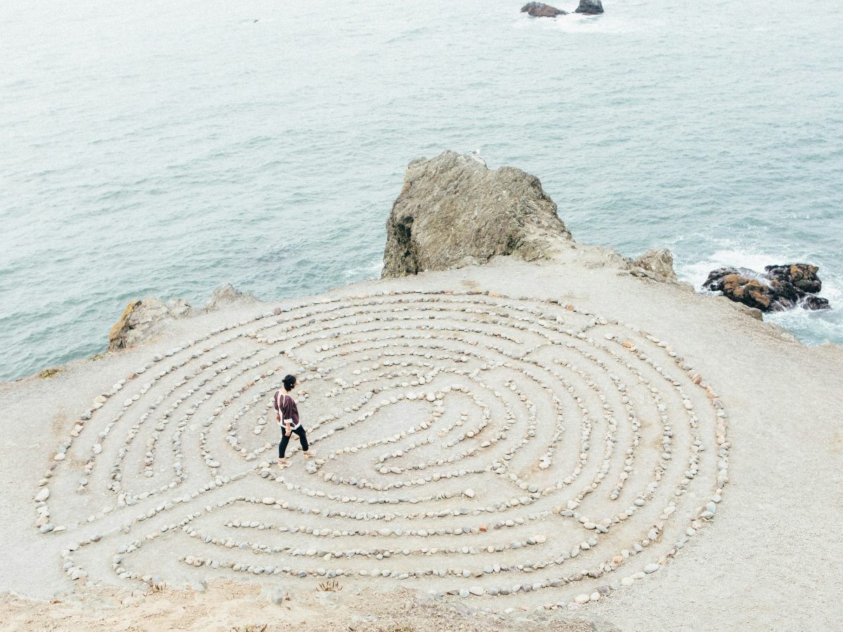 shot from aerial view, a person walking amid a design made on beach sand with the ocean as a backdrop.