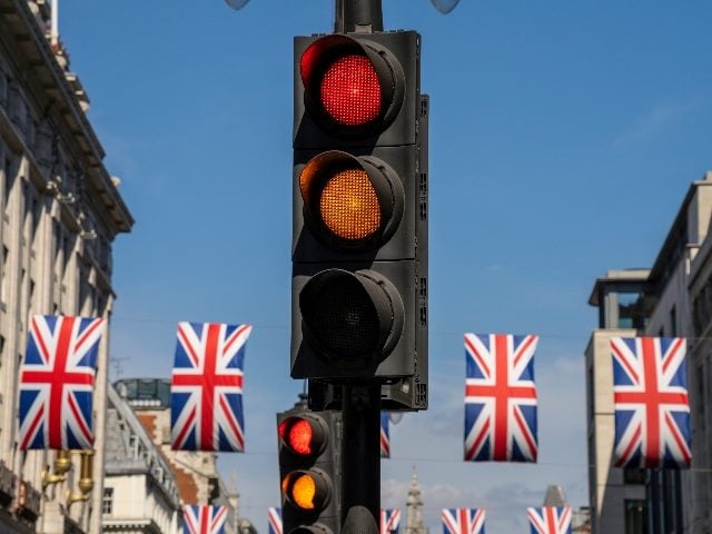 A yellow and red traffic light on a city street in London, England with British flags in the background, signaling the confusing, mixed signals CMOs give on marketing technology spending. 
