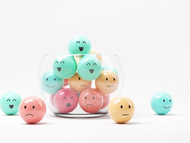 A collection of emoji emoticons are piled into a glass bowl and some are overflowing onto the surface of a table  in red, yellow, orange and blue colors, indicating the importance of customer reviews. 