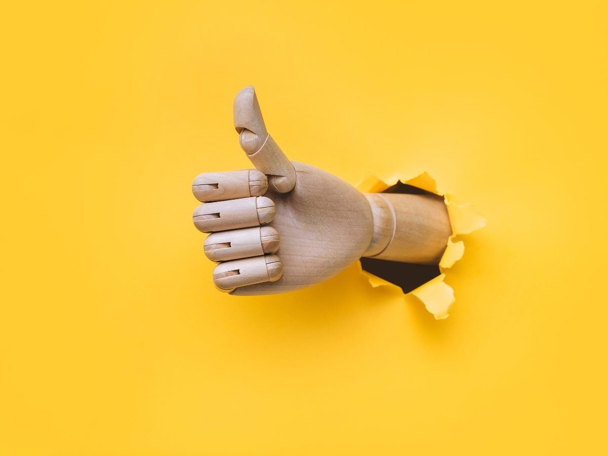 A robotic hand with the thumbs up bursting out of a yellow wall.