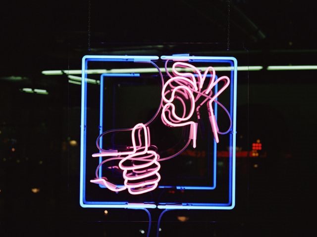 A neon sign with two hands making a thumbs up and "ok" sign