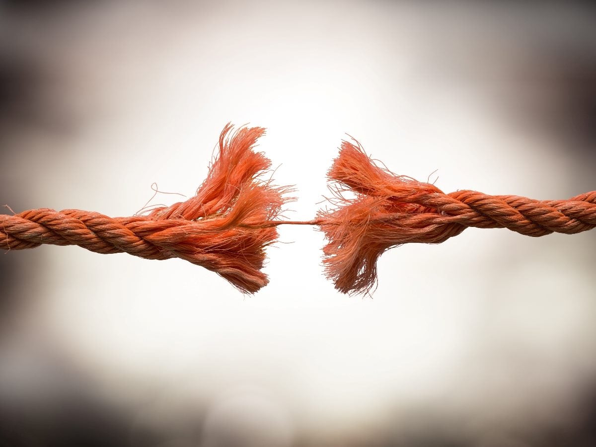 A close-up image of a thick orange rope fraying and splitting apart at the center, symbolizing organizational disconnect, broken collaboration or separation between teams and systems.