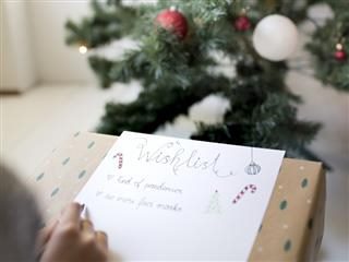 Young child's hands writing Christmas wishlist in front of a Christmas tree