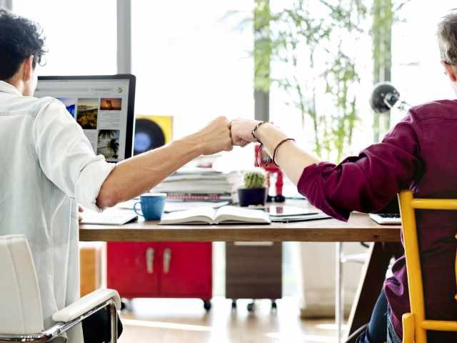 coworkers at their workstations bumping fists