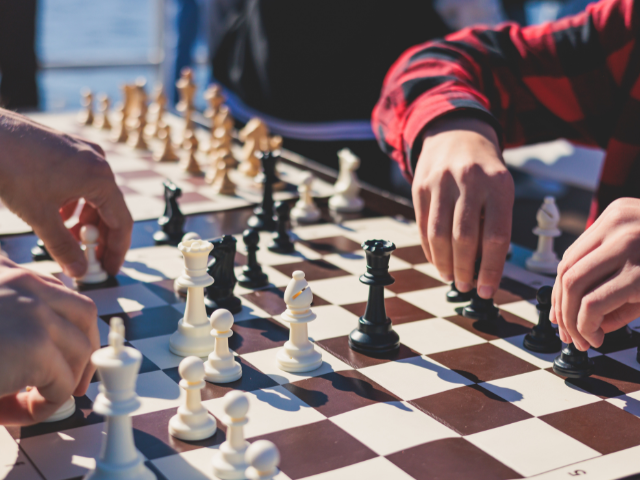 Two pairs of hands moving chess pieces on a chess board 