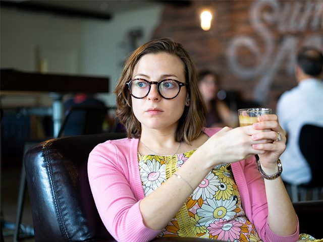 Woman holding coffee looking introspectively in the distance. 