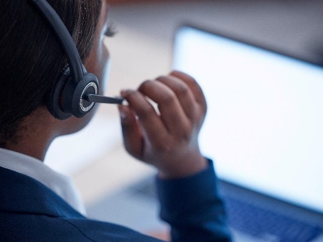 An employee wearing a suit talks to a customer in a contact center using a VOIP headset while working in front of a computer screen in piece about AI in CX and Customer Service. 