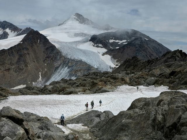 Four people walking through snowy mountains.