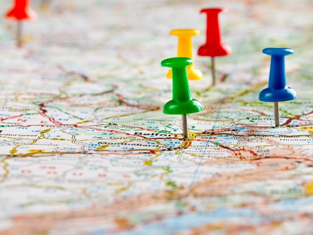 A roadmap with red, yellow, blue and green pushpins inserted into various locations in piece about digital commerce strategy road maps. 