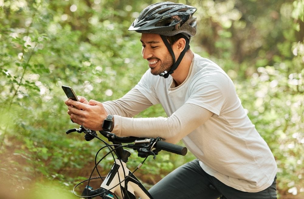 A person wearing a helmet sits on their bike while looking at their smartphone with greenery in the background in piece about real-time data.