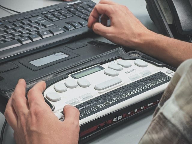 man using a braille reader keyboard with his computer
