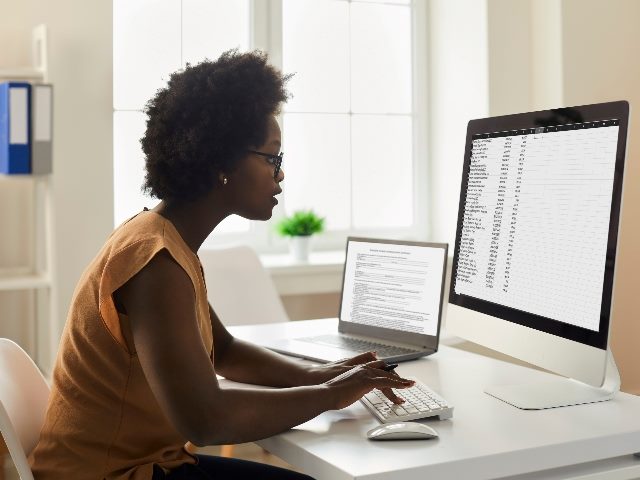 Woman looking at desktop PC screen, doing research, studying data reports.