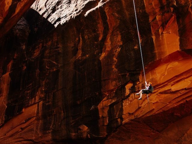 person hanging on a rope, descending into a cave