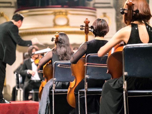 Three musicians playing violin with a conductor to their left. 