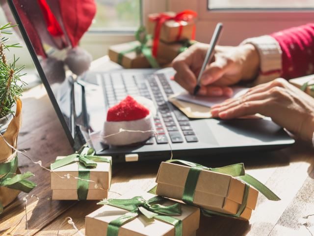 A locked down Christmas shopper buying gifts online and writing cards at their desk - Holiday Shopping