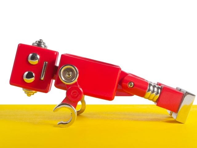 A red and silver  robot does a pushup on a bright yellow floor with white background wall, suggesting the power of AI in SEO. 