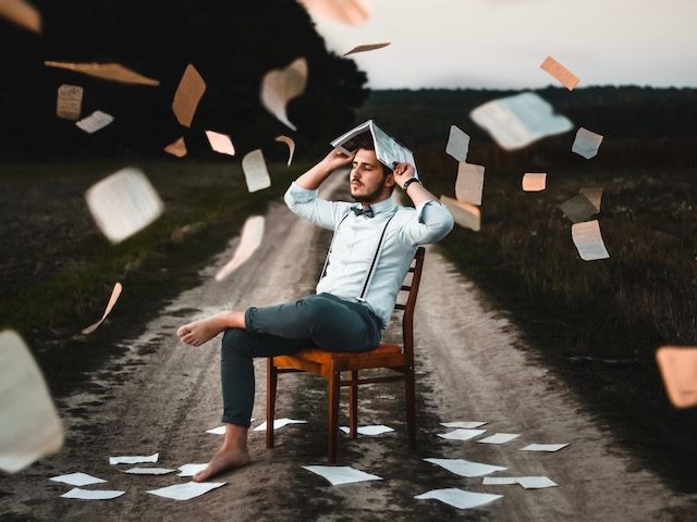 man protecting his head from paper flying around with a book