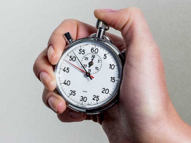 A person holds a silver stopwatch in hand with thumb ready to depress top button im piece about real-time data. 