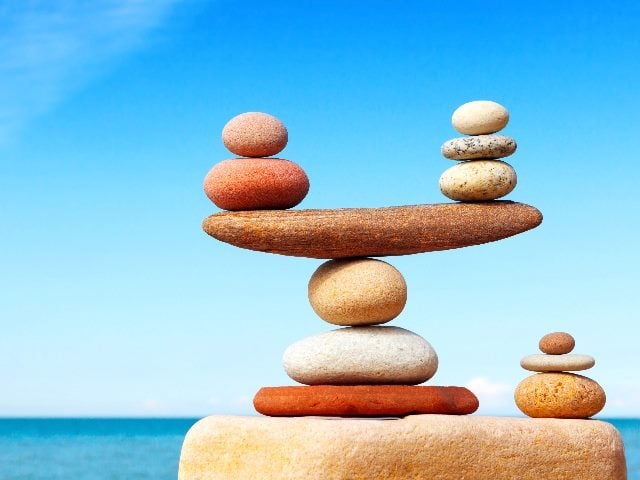 The concept of harmony and balance illustrated through a stack of stone balancing together against a blue sea and blue skies in the background in piece about harmonizing research for customer understanding. 